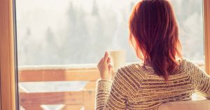 A woman is sitting, drinking coffee and looking out the window.